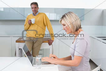Woman using laptop and man with coffee cup at kitchen