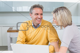 Happy casual couple using laptop in kitchen