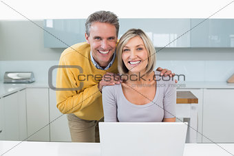 Happy casual couple with laptop in kitchen