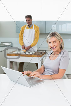 Woman using laptop and man chopping vegetables