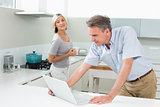 Man using laptop while woman in the kitchen