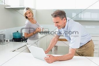 Man using laptop with woman in the kitchen