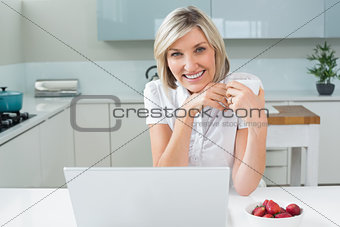 Casual woman with coffee cup and laptop in kitchen