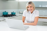 Casual happy woman with laptop in kitchen