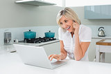 Casual woman using laptop while on call in kitchen