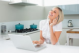 Cheerful woman using laptop while on call in kitchen