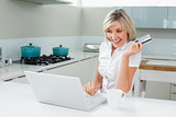 Cheerful woman doing online shopping in the kitchen