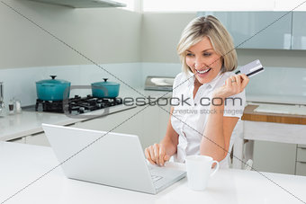 Cheerful woman doing online shopping in the kitchen