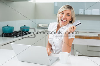 Cheerful woman doing online shopping in kitchen
