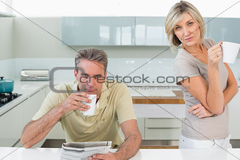 Serious couple with coffee cups and newspaper in kitchen