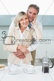 Man embracing a happy woman from behind in kitchen