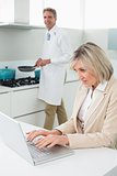 Woman using laptop and man cooking food