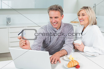Couple in bathrobes doing online shopping in kitchen