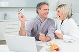 Couple in bathrobes doing online shopping in kitchen