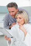 Serious couple in bathrobes reading newspaper