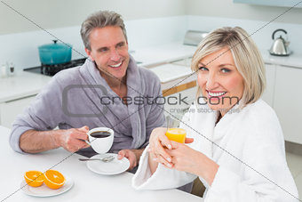 Happy couple in bathrobes having breakfast in kitchen