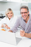 Cheerful couple in bathrobes using laptop in kitchen