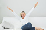 Cheerful woman sitting on sofa with arms outstretched at home