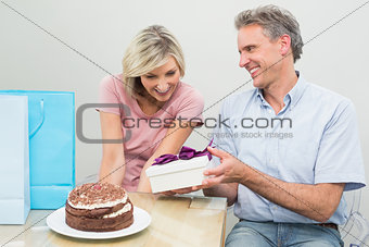Man giving a happy woman a birthday gift beside cake