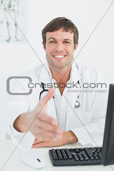 Male doctor offering a handshake at medical office desk