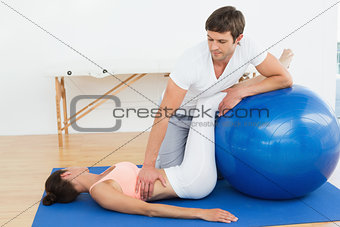 Physical therapist assisting woman with yoga ball