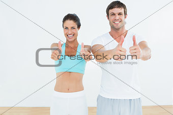 Happy fit couple gesturing thumbs up in fitness studio