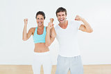 Cheerful fit couple clenching fists in fitness studio