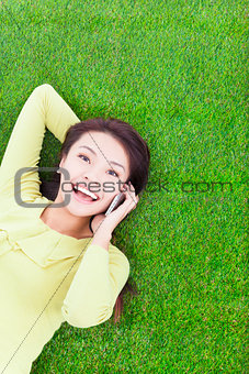smiling young woman lying with cell phone on green meadow