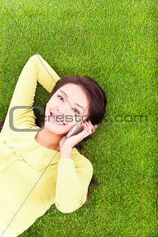 Woman smiling happily on a phone while lying grassland