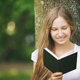 young teenage girl reading book near tree
