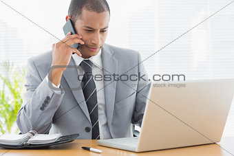 Businessman using laptop and cellphone at office