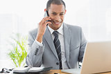Smiling businessman using laptop and cellphone