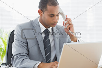 Concentrated businessman using laptop and phone