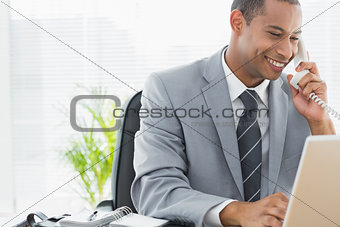 Smiling businessman using laptop and phone