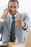 Smiling businessman gesturing thumbs up while on call