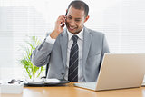 Smiling businessman with laptop using cellphone