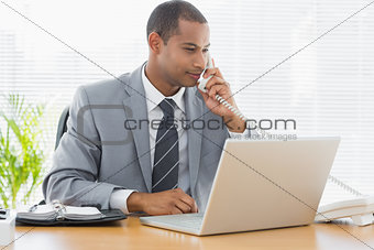 Businessman using laptop and phone at desk