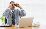 Businessman with binoculars in front of laptop at office