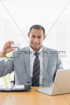 Confident well dressed man with business card at office desk