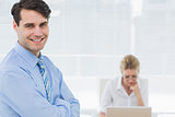 Smiling confident businessman with woman behind at office