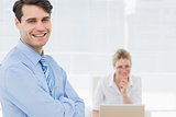 Smiling businessman with woman working behind at office