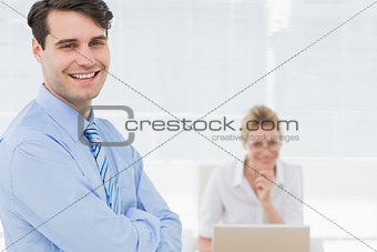 Smiling businessman with woman working behind at office
