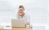 Businesswoman using laptop and phone at desk