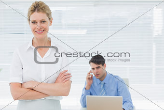 Smiling businesswoman with man working behind at office