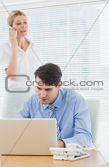 Businesswoman and man using cellphone and laptop at office