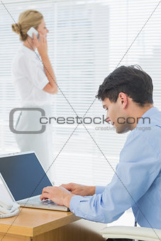 Businesswoman and man using cellphone and laptop at office