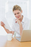 Smiling businesswoman with laptop and document at desk