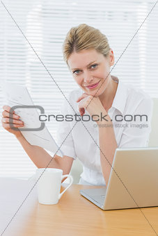 Smiling businesswoman with laptop and document at desk