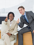 Business colleagues gesturing thumbs up in office