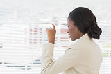Businesswoman peeking through office blinds